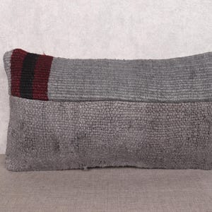 Op de afbeelding: Rechthoekig grijs kussen met een getextureerd oppervlak. Het bovenste gedeelte heeft een geweven ontwerp met een bordeauxrode en zwarte streep. Het kussen is waarschijnlijk gemaakt van een duurzame stof, geschikt voor woondecoratie.