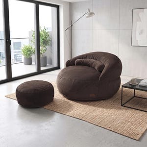 May include: A dark brown corduroy lounge chair with a rounded backrest, a matching cylindrical bolster pillow, and a separate circular ottoman. The furniture features a textured fabric surface and a small rectangular brand tag on the base.