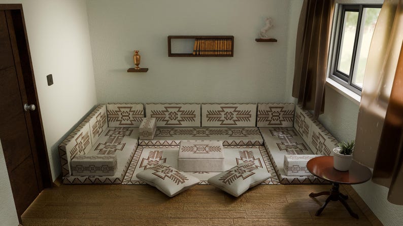 May include: A beige and brown patterned sectional sofa with matching throw pillows and a coffee table. The room has a wooden floor, a small side table, and a window with curtains. Decorative items are on the walls.
