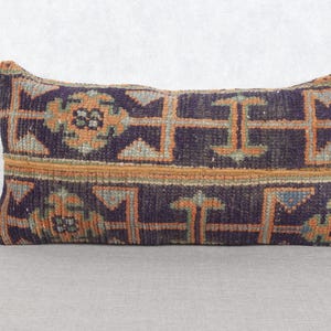 May include: Rectangular pillow with a geometric pattern in shades of navy blue, orange, and teal. The pillow has a textured appearance and a vintage aesthetic, suitable for home decor.
