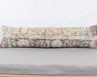 May include: A long, rectangular pillow with a vintage rug design. The pillow features a cream-colored background with faded red, black, and gray patterns. The pillow is placed on a light gray surface.