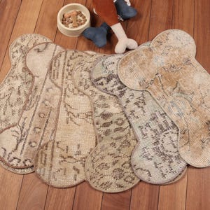 May include: A collection of bone-shaped rugs with a distressed, vintage look. The rugs are in shades of beige and brown, with intricate patterns. A dog bowl with treats and a toy are also visible.