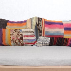 Può includere: Due cuscini rettangolari con un design patchwork. I cuscini presentano una varietà di colori tra cui arancione, rosa, viola e marrone. Il design patchwork include strisce e tessuto fantasia.