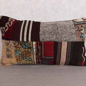 May include: Rectangular patchwork pillow with a variety of patterned fabric sections. The pillow features sections of beige, brown, red, and black fabrics with geometric and striped designs. A decorative accent for a sofa or bed.