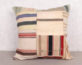 May include: Square patchwork pillow with a variety of fabric patterns and colors. The pillow features stripes in red, black, and white, as well as other neutral tones. The pillow is a decorative item for a bed or sofa.