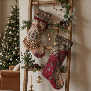 May include: Two decorative Christmas stockings hanging on a wooden ladder. The left stocking features a beige, red, and blue intricate medallion pattern. The right stocking displays a deep red and green floral motif. Both have hanging loops.