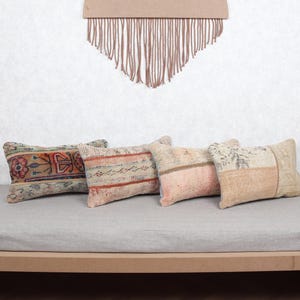 Puede incluir: Cuatro cojines rectangulares con diseños estampados en colores apagados como beige, rosa y óxido están dispuestos sobre una superficie gris claro. Los cojines tienen una estética vintage y bohemia, adecuada para la decoración del hogar.