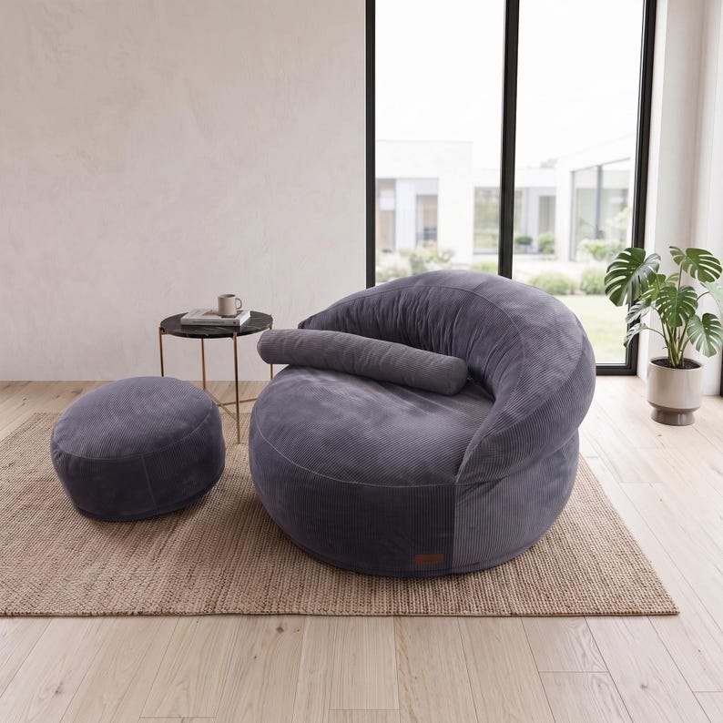 May include: A dark gray corduroy bean bag chair with a matching cylindrical bolster pillow and a separate round ottoman. The furniture features a textured ribbed fabric finish and a rounded, low-profile design for seating comfort.