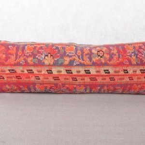 Puede incluir: Cojín rectangular largo con un patrón detallado y colorido. Predominan los tonos rojos, naranjas y morados, con elementos florales y geométricos. El estilo del cojín evoca una estética textil vintage o étnica.