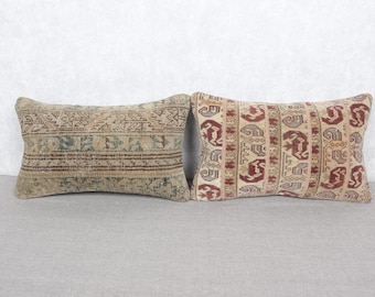 May include: Two rectangular throw pillows with patterned designs. One pillow features a beige background with a geometric pattern in shades of brown and teal. The other pillow has a beige background with a repeating red and gray motif.
