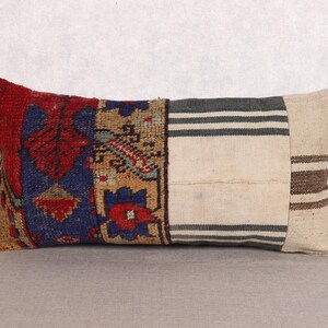 May include: Rectangular decorative pillow with a patchwork design. The pillow features sections of red, blue, and tan patterned fabric, along with striped and solid neutral-toned sections. The pillow is designed for home decor.