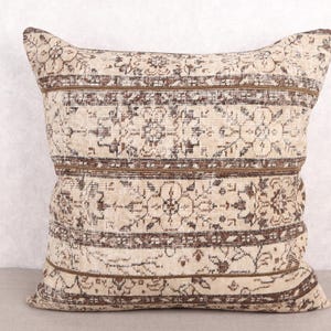 May include: A square decorative pillow with a vintage-style design. The pillow features a cream-colored background with brown floral and geometric patterns. Brown stripes run horizontally across the pillow, adding to its antique aesthetic.