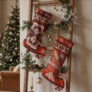 Könnte beinhalten: Zwei Weihnachtsstrümpfe mit einem gewebten, mehrfarbigen geometrischen Muster in Rot-, Marineblau- und Cremetönen. Die Strümpfe hängen an einer Holzleiter, die mit Tannenzweigen, kleinen Glocken und Glaskugeln geschmückt ist.