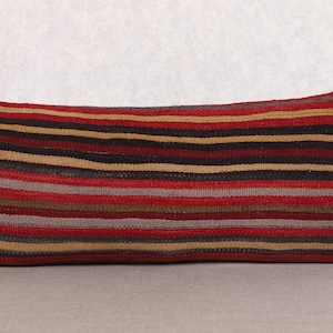 Puede incluir: Cojín rectangular con un diseño de rayas en tonos rojos, marrones, beige y grises. El cojín tiene una forma ligeramente curvada y probablemente está hecho de tela tejida. Este cojín decorativo se puede usar en un sofá o cama.