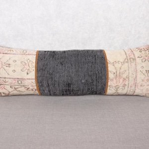May include: Rectangular decorative pillow with a central dark gray section and patterned ends. The ends feature a cream background with pink and beige floral designs. A thin brown border separates the sections. The pillow is on a gray surface.