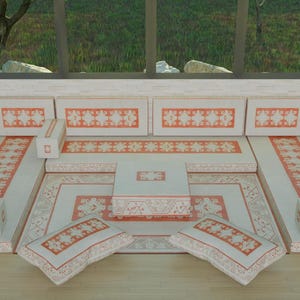 Puede incluir: Una zona de estar color crema con detalles estampados en naranja. El conjunto incluye una alfombra grande, cojines y bancos empotrados. Una pequeña mesa cuadrada se encuentra en el centro. La habitación tiene una ventana con vistas a la vegetación.