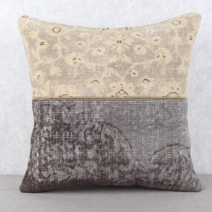May include: A decorative pillow with a two-tone design. The top half features a beige floral pattern, while the bottom half has a dark gray and brown abstract design. The pillow is rectangular and appears to be made of a woven fabric.