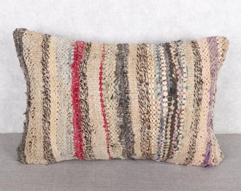 Può includere: Cuscino rettangolare tessuto con un motivo a righe. Il cuscino presenta strisce verticali beige, rosse, grigie e viola. La trama appare ruvida e fatta a mano, adatta all'arredamento.
