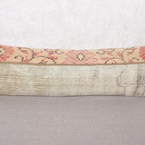 May include: A long, rectangular cushion with a beige and red floral design on the top. The lower section is a lighter beige with faded patterns. The cushion is placed on a grey surface.