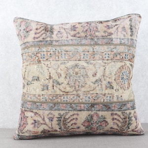 May include: Square decorative pillow with a vintage rug design. The pillow features a beige background with floral and geometric patterns in shades of pink, blue, and brown. The pillow is a square shape.