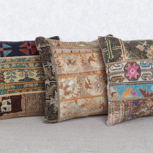 May include: Three square throw pillows with a patchwork design. The pillows feature a variety of colors, including blue, brown, beige, and pink. The pillows appear to be made from a woven fabric, possibly a rug or tapestry.