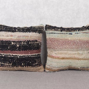 Puede incluir: Dos almohadas decorativas con un patrón tejido. Las almohadas están hechas de una tela suave y texturizada y presentan una mezcla de rayas negras, blancas, marrones y rosas.