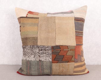 May include: A square patchwork pillow with a variety of neutral-toned fabric squares. The pillow features a mix of textures and patterns, including stripes, geometric designs, and woven fabrics. The color palette includes beige, brown, orange, and gray.