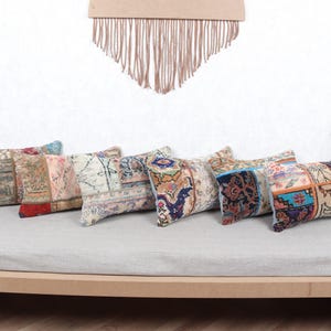 Könnte beinhalten: Eine Sammlung rechteckiger Zierkissen mit Patchwork-Designs in verschiedenen Farben, darunter Rot, Grün, Blau und Beige. Die Kissen sind auf einer hellgrauen Oberfläche angeordnet, mit einem dekorativen Wandbehang im Hintergrund.
