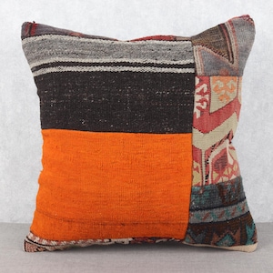May include: Square decorative pillow with a patchwork design. The pillow features a vibrant orange section, a dark brown section, and a section with a patterned design in red, beige, and blue. The pillow is a home decor item.