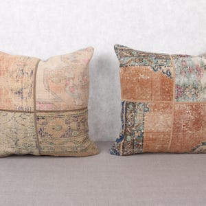 May include: Two decorative throw pillows with a patchwork design. The pillows feature a mix of colors, including beige, peach, and blue, with intricate patterns reminiscent of vintage rugs. The pillows are rectangular and appear to be made of a soft fabric.