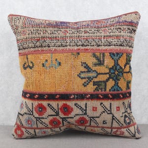 Pode incluir: Almofada decorativa quadrada com um design vintage estampado. A almofada apresenta um esquema de cores bege, laranja e vermelho com motivos geométricos e florais. As seções superior e inferior têm uma textura tecida.