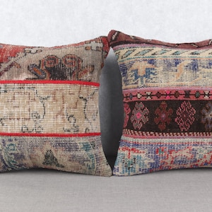 Op de afbeelding: Twee vierkante decoratieve kussens met een vintage patchwork ontwerp. De kussens hebben een mix van kleuren, waaronder rood, beige, blauw en bruin. De kussens hebben een getextureerde, geweven uitstraling, wat wijst op een tapijt- of textieloorsprong.