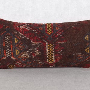 Puede incluir: Cojín decorativo rectangular con un diseño tejido y estampado. El cojín presenta un fondo marrón oscuro con formas geométricas rojas, amarillas y blancas. Es un artículo de decoración para el hogar.