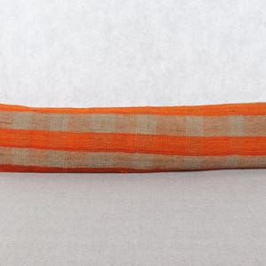 May include: A long, rectangular pillow with a striped pattern. The pillow features alternating bands of orange and tan. The pillow is made of a woven fabric and is likely used for decorative purposes on a bed or sofa.