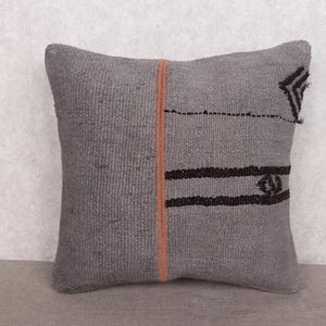 May include: Gray square pillow with a woven texture. A vertical orange stripe runs down the center, with dark brown geometric patterns on the right side. The pillow is a neutral color, suitable for various decor styles.
