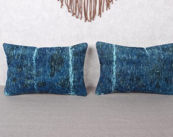 May include: Two rectangular throw pillows with a distressed, textured appearance. The pillows are primarily a deep blue color with lighter blue and black accents. The pillows are placed on a gray surface.