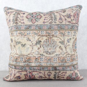 May include: Square decorative pillow with a vintage rug design. The pillow features a cream-colored background with floral and geometric patterns in shades of pink, blue, and green. The pillow is a square shape, perfect for a sofa or bed.