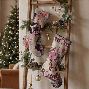 Könnte beinhalten: Zwei Weihnachtsstrümpfe hängen an einer Holzleiter. Der linke Strumpf hat eine beige Basis mit geometrischen Sternmustern in Schwarz, Pink und Türkis. Der rechte Strumpf zeigt eine beige Basis mit einem komplexen, abstrakten Muster in Pink, Türkis und Schwarz.