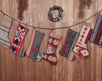 Könnte beinhalten: Eine Sammlung von Weihnachtsstrümpfen mit verschiedenen geometrischen Mustern in Rot, Blau, Grau und Beige, die an einer Schnur vor einem Holzgrund hängen. Ein kleiner Kranz ist im Hintergrund zu sehen.