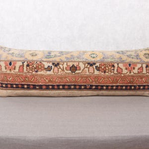 May include: Rectangular lumbar pillow with a vintage rug design. The pillow features a beige background with a central band of rust, brown, and pink floral patterns. The top and bottom borders are blue and black.