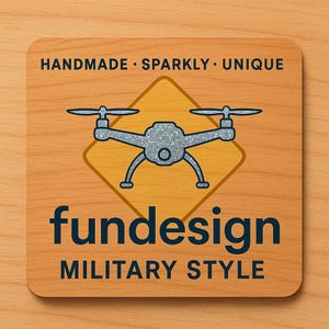Könnte beinhalten: Ein quadratisches Holzschild mit abgerundeten Ecken zeigt eine Drohnen-Grafik in einem gelben Diamanten. Das Schild trägt oben die Aufschrift "HANDMADE • SPARKLY • UNIQUE", darunter "fundesign" in Marineblau und unten "MILITARY STYLE".