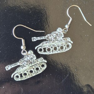 Könnte beinhalten: Ein Paar silberfarbene Panzer-Ohrringe mit Glitzer-Finish. Die Ohrringe haben einen Haken für durchbohrte Ohren. Die Panzer haben detaillierte Ketten und Türme und sind ein einzigartiges Accessoire.