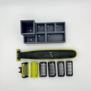 Könnte beinhalten: Ein schwarzer und gelber Elektrorasierer mit mehreren Trimmerköpfen und einem grauen Organizer. Der Rasierer hat einen schwarzen Körper mit gelbem Akzent und einen gelben Trimmerkopf. Der Organizer hat mehrere Fächer.