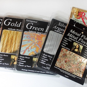 May include: A collection of crafting supplies including multiple packages of authentic metal leaf in gold, variegated green, and silver, alongside a container of metal flakes and a package of Delta Renaissance Foil for gold leafing projects.