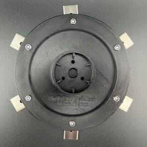 Könnte beinhalten: Ein kreisförmiger schwarzer Trimmerkopf mit sechs silbernen Metallklingen, die vom Rand abstehen. Die zentrale Nabe hat ein vertieftes kreisförmiges Design mit mehreren kleinen Löchern. Der Text "Fits McCulloch 1-1/8in 28mm" ist auf der Oberfläche eingeprägt.