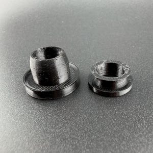 Peut inclure: Deux objets noirs imprimés en 3D. L'un est de forme cylindrique sur une base plate, l'autre est de forme similaire mais plus petit. Ce sont probablement des composants pour un assemblage plus grand, peut-être mécanique ou technologique.