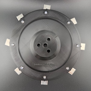 Peut inclure: Un composant mécanique noir circulaire doté d'un moyeu central avec trois trous circulaires. Le bord extérieur est fixé par huit boulons métalliques argentés régulièrement espacés, chacun retenant une petite languette métallique rectangulaire.
