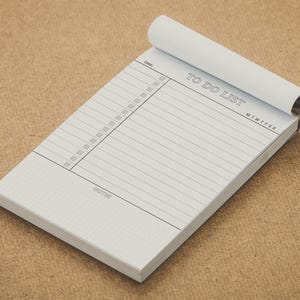 May include: A white notepad with the words "TO DO LIST" printed in grey. The notepad has a section for the date, checkboxes, and lined spaces for notes. The top pages are rolled over.
