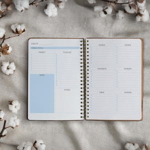 Pode incluir: Um planejador semanal com um design azul e branco. A página da esquerda tem seções para o foco semanal, a prioridade, a lista de tarefas, as notas e o rabisco. A página da direita tem seções para segunda-feira, terça-feira, quarta-feira, quinta-feira, sexta-feira e fim de semana.