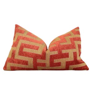 May include: A red and gold geometric patterned throw pillow. The pillow has a woven design with a geometric pattern in gold on a red background.